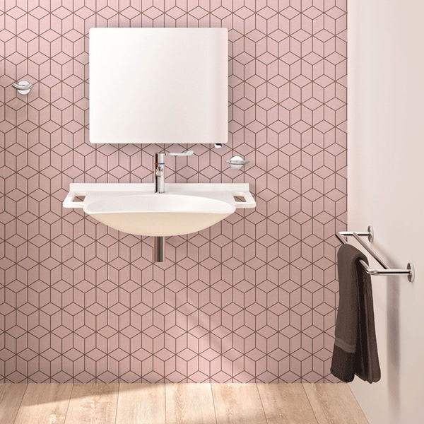 Wandhängendes weißes Waschbecken mit seitlichen Griffen, verchromter Armatur, Spiegel und Handtuchhalter vor einer Wand mit rosa Fliesen.