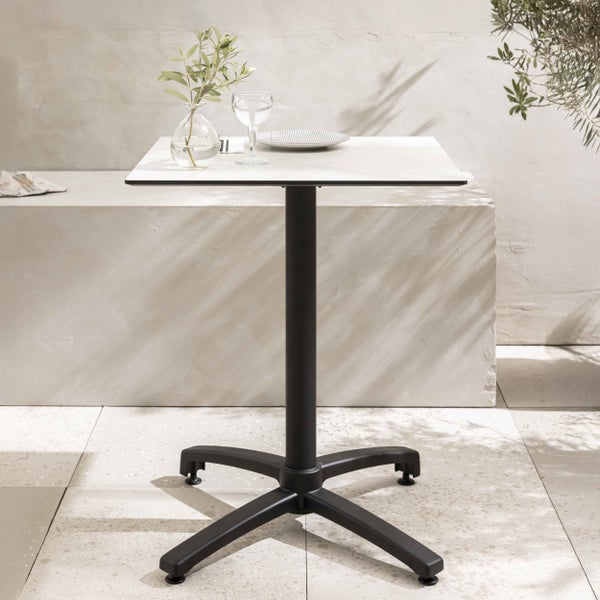 Moderner quadratischer Bistrotisch mit weißer Tischplatte und schwarzem Metallsäulenfuß auf einer hellen Terrasse.