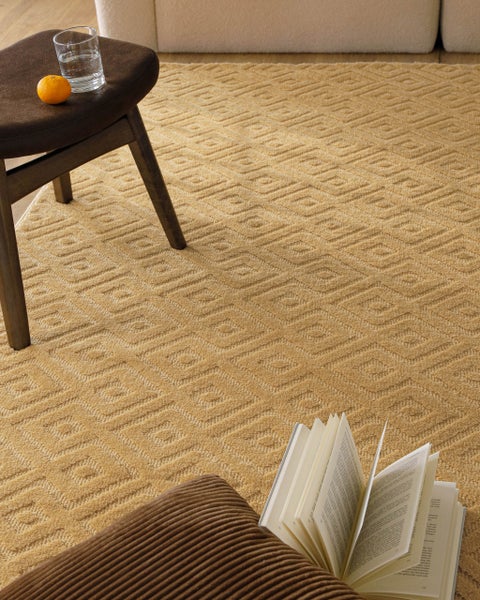 Strukturierter Teppich mit geometrischem Muster in einem hellen, organisierten Wohnzimmer mit Hocker, Buch und Cordkissen.