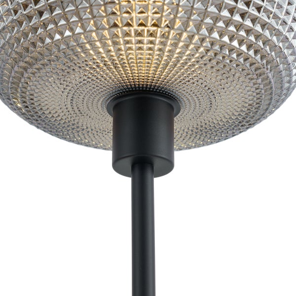 Detailansicht einer Lampe mit strukturiertem Glasschirm und mattschwarzem Metallschaft.