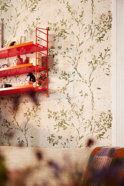 Wand mit botanischer Tapete und ein hängendes Metallregal mit Dekorationsartikeln in einem modern eingerichteten Wohnbereich.