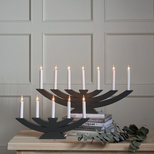 Grauer Kerzenleuchter mit elf elektrischen Kerzen auf einem Holztisch, dekoriert mit Büchern und Eukalyptusblättern.