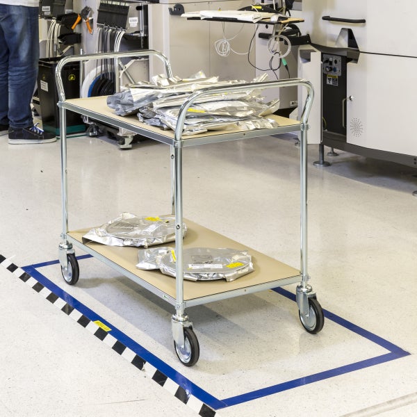 Ein Transportwagen mit zwei Ablageflächen, beladen mit verpackten Produkten in einer Industrieumgebung.