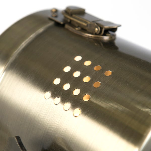 Detailaufnahme einer zylindrischen Leuchte in Antikoptik mit einem metallischen Verschluss und einem quadratischen Lochmuster.
