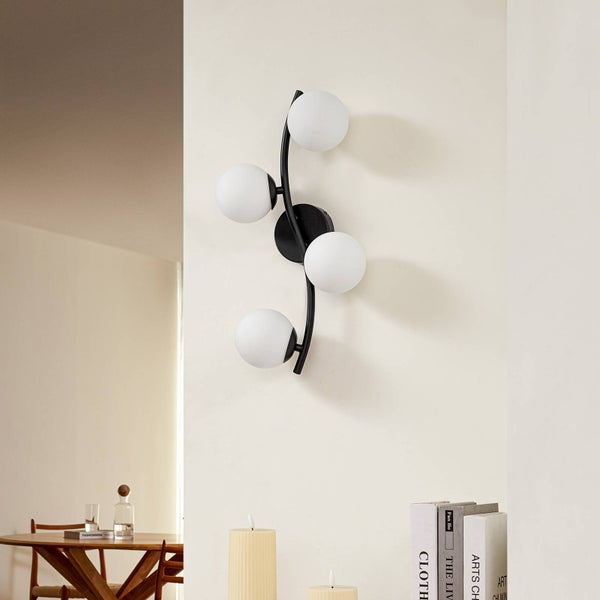 Wandleuchte mit vier weißen Kugellampen an einer geschwungenen, schwarzen Halterung.