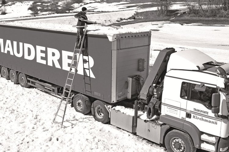 Mann auf einer Leiter beim Schneeräumen von einem Lastwagen