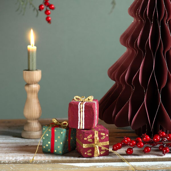Weihnachtliche Tischdekoration mit einem Papierbaum, kleinen Geschenkpaketen, einem Kerzenhalter aus Holz mit brennender Kerze und roten Beeren.