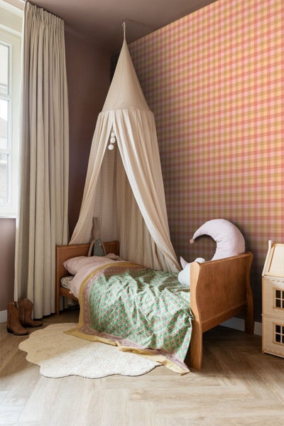 Kinderzimmer mit Vliestapete im Vichy-Karo-Muster, Holzbett mit Betthimmel und hellen Vorhängen.
