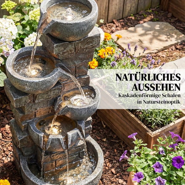 Eine Frau meditiert auf einer hellen Terrasse neben einem mehrstufigen Gartenbrunnen in Steinoptik mit fließendem Wasser und Pflanzen.