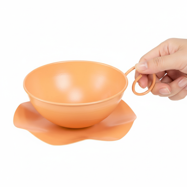 Oranges Pflanzgefäß aus Metall in Form einer Tasse mit Untertasse, von einer Hand am Griff gehalten.