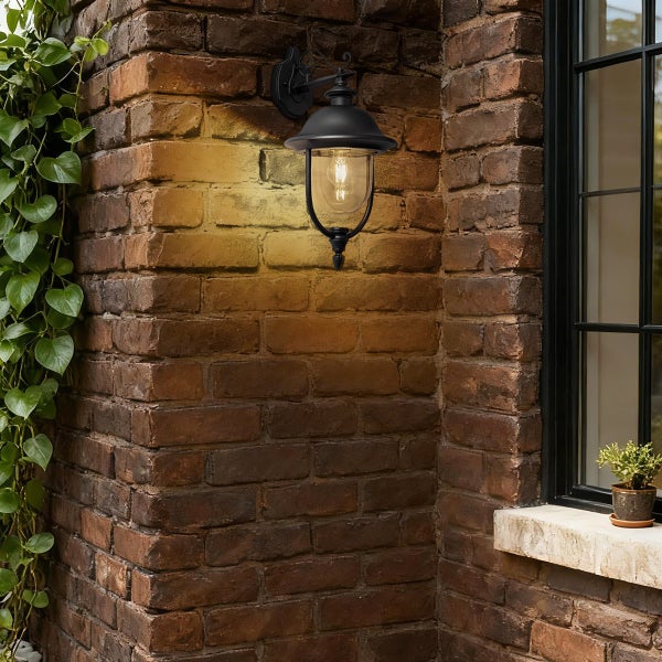 Schwarze Außenwandleuchte im Laternen-Stil an einer Ziegelwand montiert, beleuchtet mit warmem Licht.