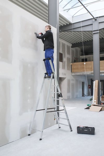 Handwerker steht auf einer Aluminium Stehleiter und verspachtelt eine Gipskartonwand in einem Rohbau.