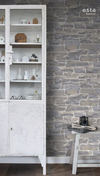 Helles Zimmer mit einer Mauerwerk-Tapete, die eine rustikale Atmosphäre schafft. Ein weißer Schrank mit Glasfront zeigt dekorative Gegenstände.