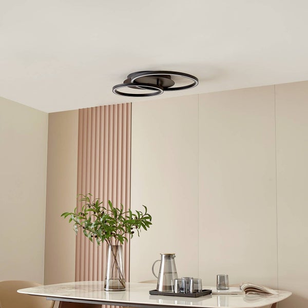 Moderne LED-Deckenleuchte mit drei überlappenden schwarzen Ringen in einem hellen Esszimmer über einem weißen Tisch mit Vase.