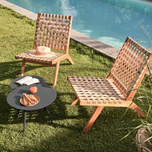 Zwei Garten-Loungesessel aus Holz mit Geflecht-Sitzfläche und ein kleiner runder Beistelltisch auf einer Rasenfläche neben einem Swimmingpool.