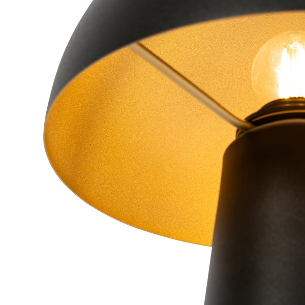 Nahaufnahme einer Lampe mit schwarzem Schirm, goldfarbener Innenseite und leuchtendem Leuchtmittel.