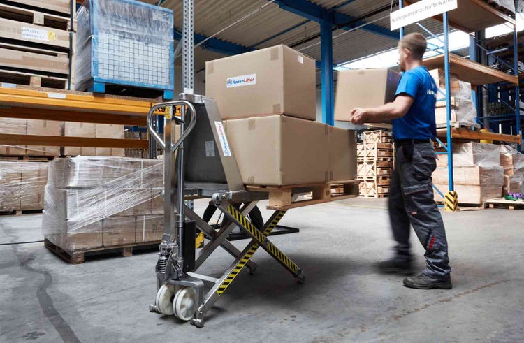 Mitarbeiter belädt einen HanseLifter Scherenhubwagen mit Kartons in einem organisierten Lager.
