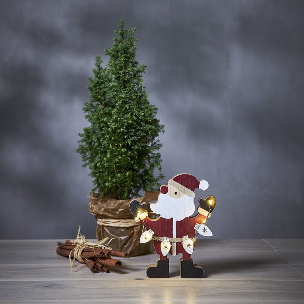 Dekoratives Weihnachtsstilleben mit kleinem Baum, Zimtstangen und beleuchteter Weihnachtsmannfigur