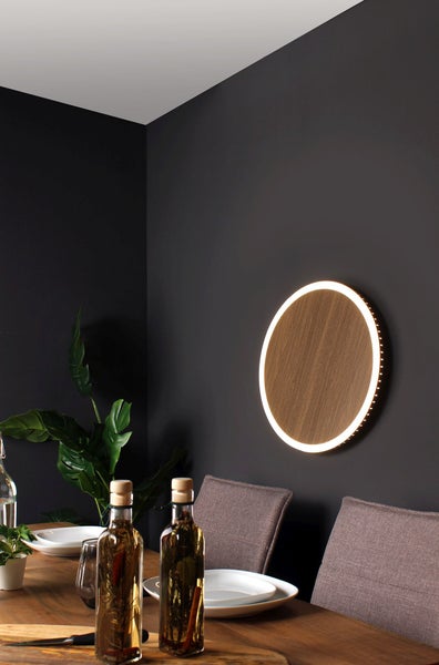 Runde LED-Wandleuchte mit Holzdekor an einer dunkelgrauen Wand in einem modern eingerichteten Esszimmer.