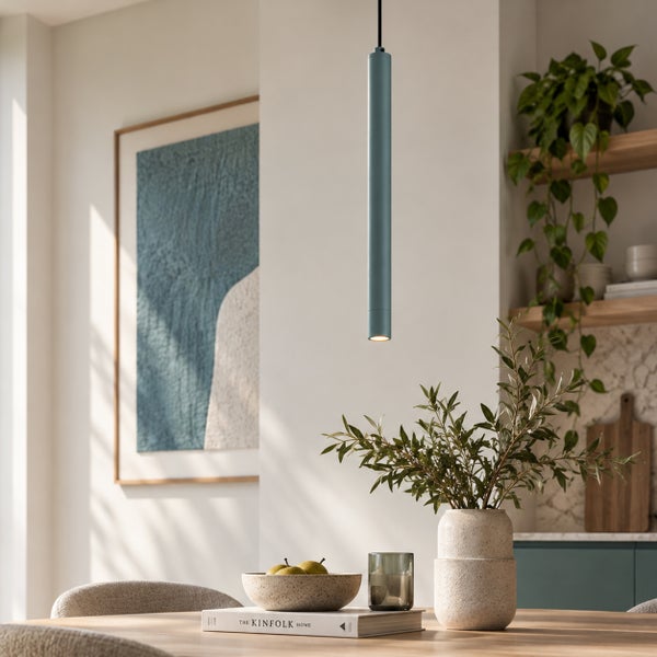 Moderne zylindrische Pendelleuchte über einem Holzesstisch in einem hellen, wohnlich eingerichteten Essbereich mit Zimmerpflanzen und Wandkunst.
