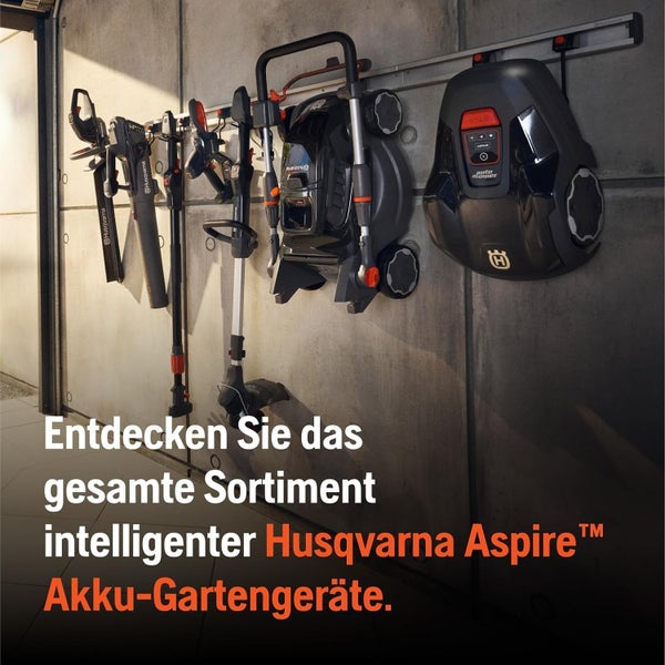Husqvarna Aspire Akku Gartengeräte Sortiment an einer Garagenwand hängend