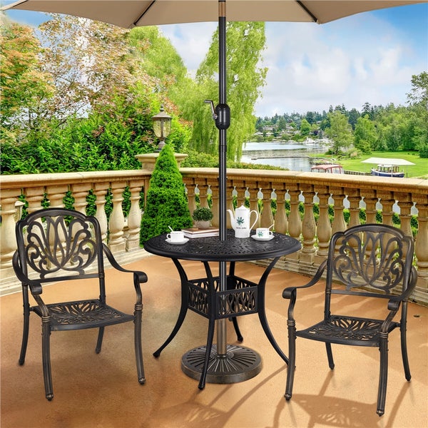 Gartenmöbel-Set bestehend aus zwei verzierten Metallstühlen und einem runden Tisch mit Sonnenschirm auf einer Terrasse mit Seeblick.