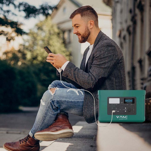Mann sitzt draußen und lädt sein Telefon mit einer tragbaren V-TAC Powerstation auf.