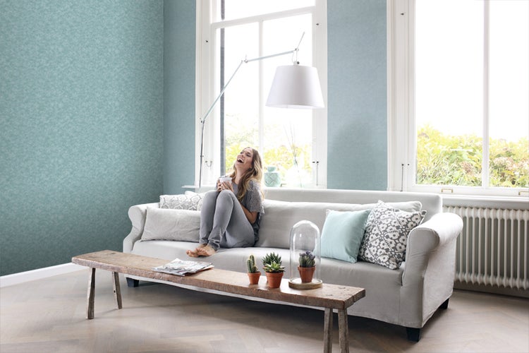 Wohnzimmer mit hellblauer Tapete, Sofa, Holztisch und lachender Frau