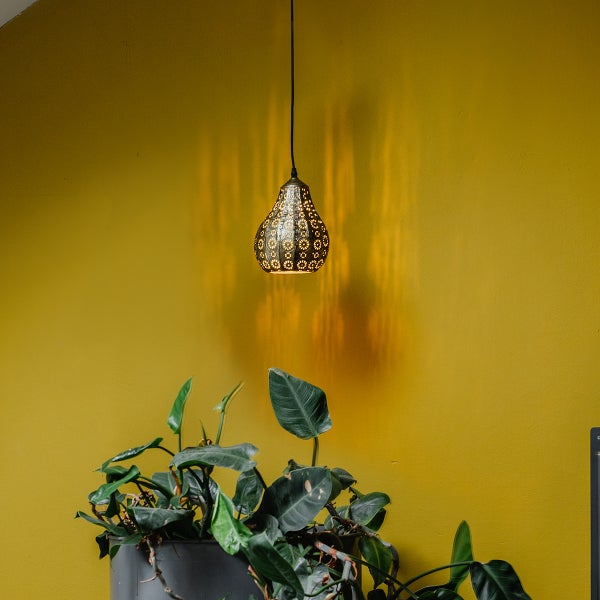 Hängeleuchte mit floralem Muster und dekorativem Lichteffekt über einer Zimmerpflanze