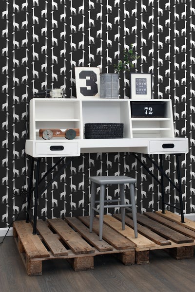 Weißer Schreibtisch mit schwarzen Beinen und grauem Hocker vor einer Wand mit Giraffenmuster.