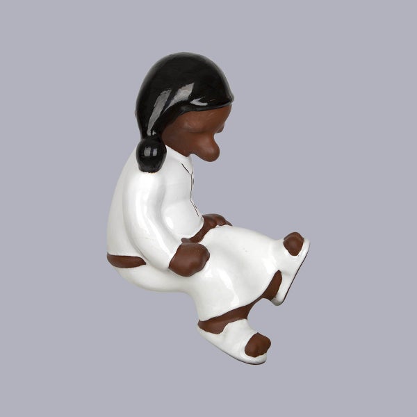 Dekorative Keramikfigur einer sitzenden Person in weißer Kleidung mit schwarzer Kopfbedeckung.