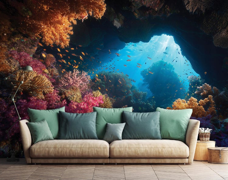 Wohnzimmer mit Tapete, die eine Unterwasserlandschaft mit Korallen und Fischen darstellt, darüber ein beiges Sofa mit grünen Kissen.