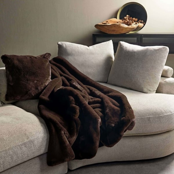 Dekorative Szene mit brauner Kunstfell-Decke und passendem Kissen auf einem Sofa.