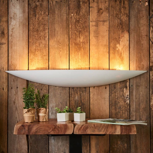 Weiße sichelförmige Wandleuchte für indirekte Beleuchtung an einer rustikalen Holzwand über einem Regal mit kleinen Pflanzen.
