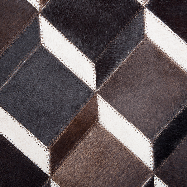 Detail eines Patchwork-Teppichs aus echtem Kuhfell mit geometrischem Würfelmuster und dekorativen Zickzacknähten.