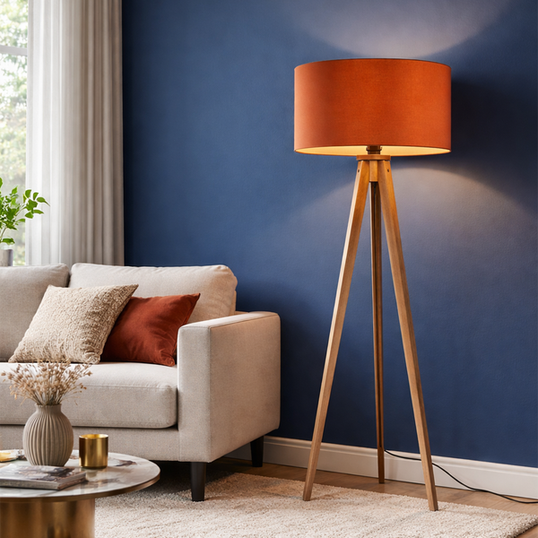 Moderne Stativ Stehleuchte mit Holzbeinen und zylindrischem Lampenschirm in einem Wohnzimmer mit Sofa und Couchtisch.