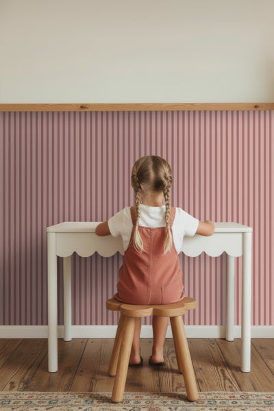 Vliestapete mit Streifenmuster im Kinderzimmer, kombiniert mit weißem Kinderschreibtisch und hölzernem Hocker.