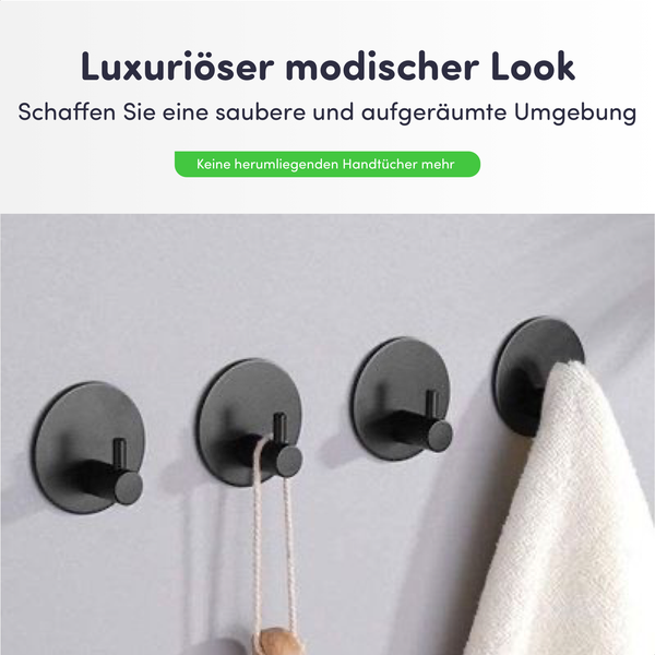 Vier runde, selbstklebende Handtuchhaken aus schwarzem Metall an einer Wand montiert, einer hält ein weißes Handtuch.