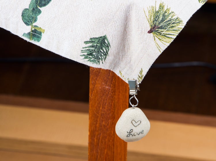 Tischdeckengewicht in Steinoptik mit Herzmotiv und der Aufschrift Love befestigt an einer Tischdecke mit Naturmotiven