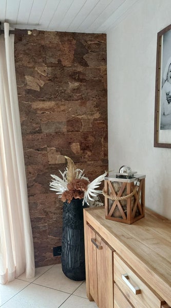 Wand mit natürlichen Kork-Wandpaneelen in einem Wohnraum neben einem hellen Holz-Sideboard und einer schwarzen Vase mit Dekoration.
