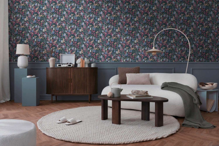 Wohnzimmer mit dunkler Blumentapete, weißem Sofa, Holztisch und Fischgrätparkett. Ein stilvoll eingerichteter Raum mit moderner Wandgestaltung.