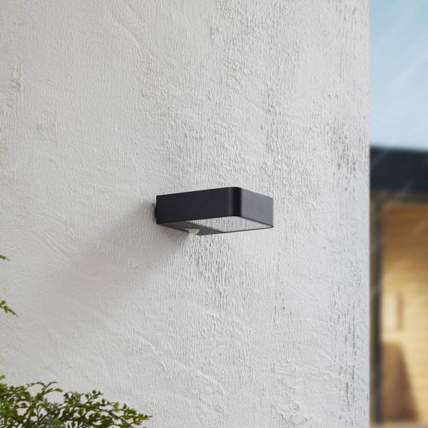 Moderne schwarze Außenwandleuchte mit Bewegungsmelder an einer strukturierten Wand.