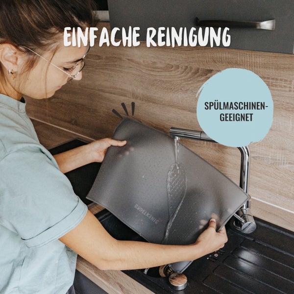 Eine Person reinigt eine Rudelkönig Schneidematte unter fließendem Wasser in einer Küchenspüle. Die Schneidematte ist spülmaschinengeeignet.