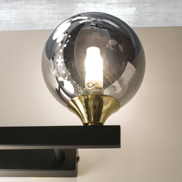 Wandleuchte mit einer runden, grauen Glaskugel und einer goldenen Fassung auf einem schwarzen Sockel