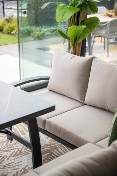 Modernes Garten-Lounge-Set mit beigen Polstern, schwarzem Gestell und einem Beistelltisch in Marmor-Optik auf einer hellen Terrasse.