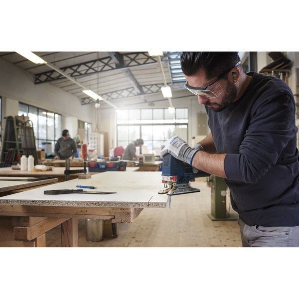 Ein Handwerker sägt mit einer Stichsäge ein Werkstück in einer Werkstatt.