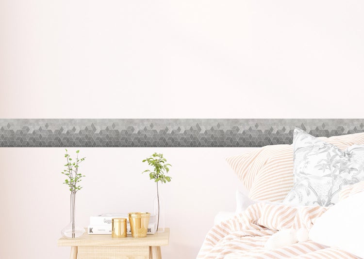 Tapetenbordüre mit geometrischem Würfelmuster an einer Wand im Wohnbereich neben einem Sessel und einem Beistelltisch.