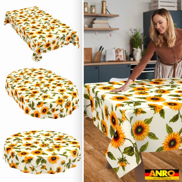 Abwaschbare Tischdecke mit Sonnenblumenmuster in rechteckig, oval und rund. Frau deckt Holztisch in heller Küche. ANRO Deutsche Manufaktur Logo.