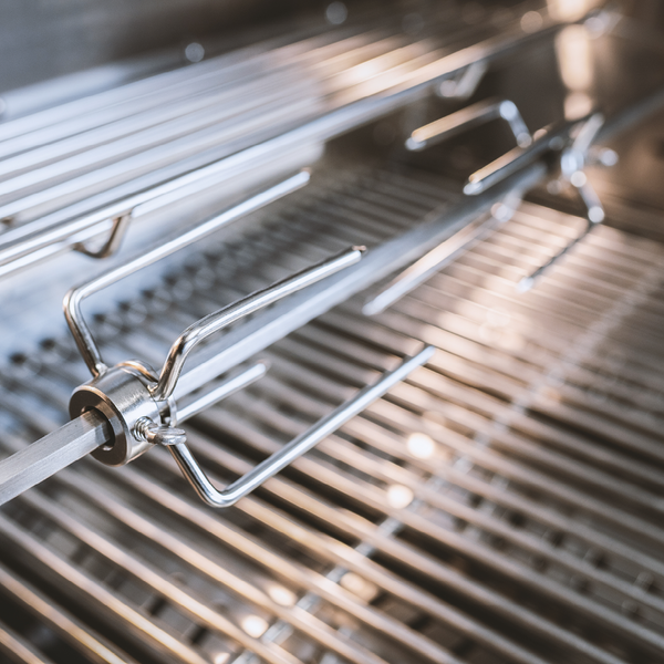 Rotisserie-Grillspieß aus Edelstahl mit Fleischklammern im Inneren eines Grills.