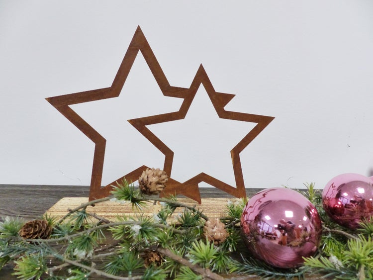 Weihnachtsdekoration mit zwei Sternen aus Metall in Edelrostoptik auf einem Holzsockel, dekoriert mit Tannenzweigen, Zapfen und Weihnachtskugeln.